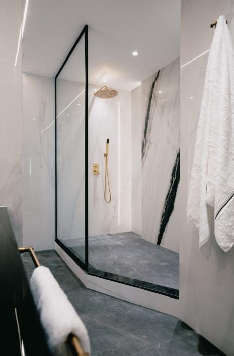 Walk-in shower framed in black steel against veined stone